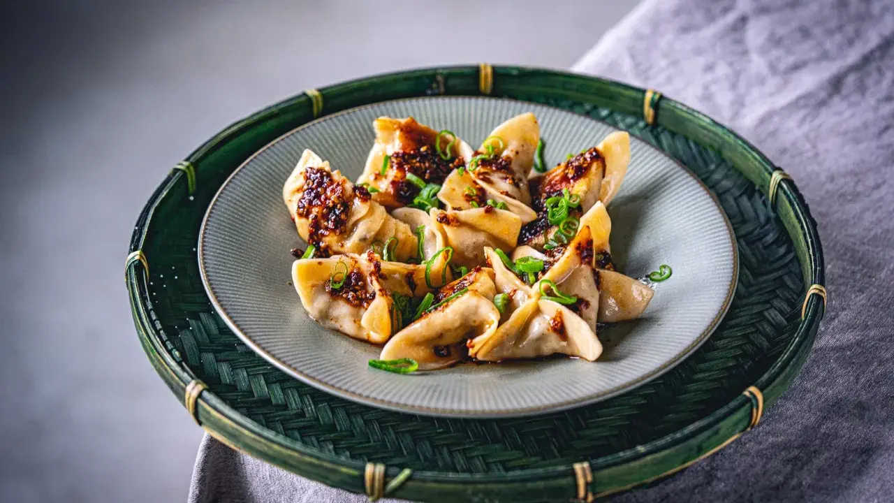 Gyoza vegetarisch, appetitlich mit würziger Soße und Frühlingszwiebeln garniert, auf einem Teller in einem grünen Bambuskorb serviert.