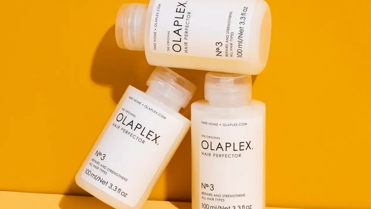 Drei Flaschen der OLAPLEX Serie, "Hair Perfector No.3", liegen übereinander auf einem orangen Hintergrund.