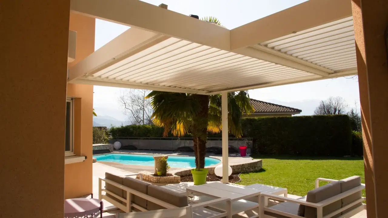 Une pergola bioclimatique moderne avec des lames orientables protège un salon extérieur et une piscine.