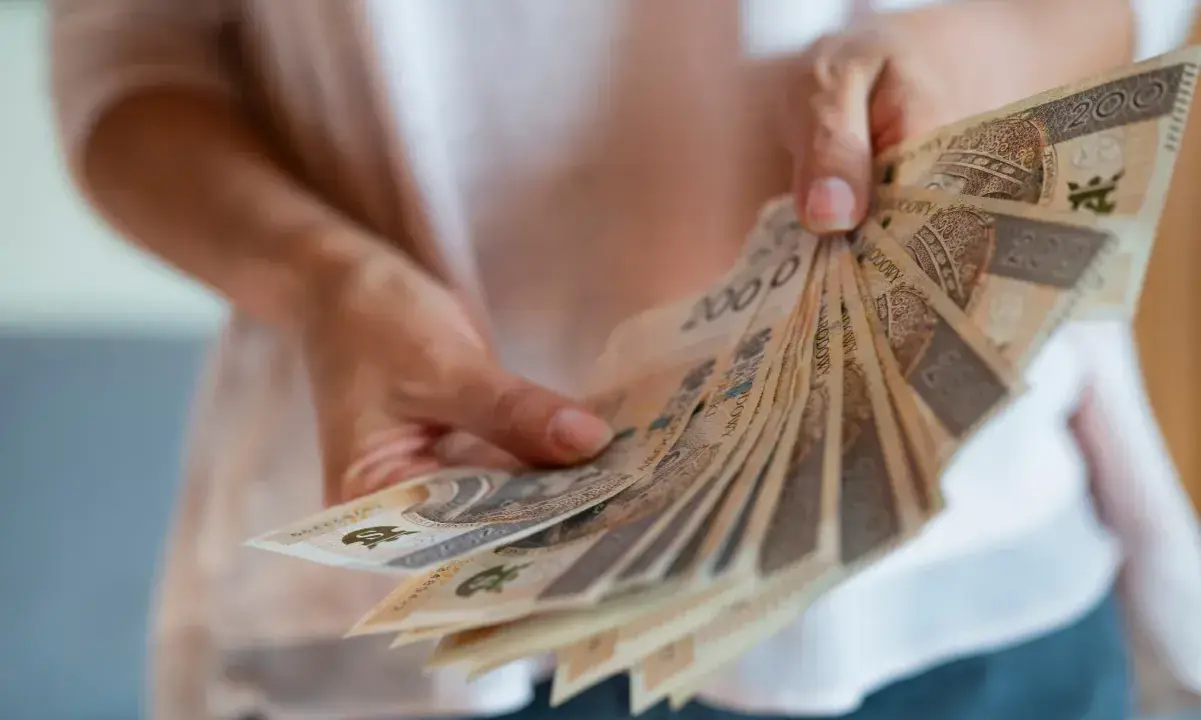 Dłonie trzymają wachlarz polskich banknotów. Zastanawiasz się, czy nagroda jubileuszowa wlicza się do emerytury?