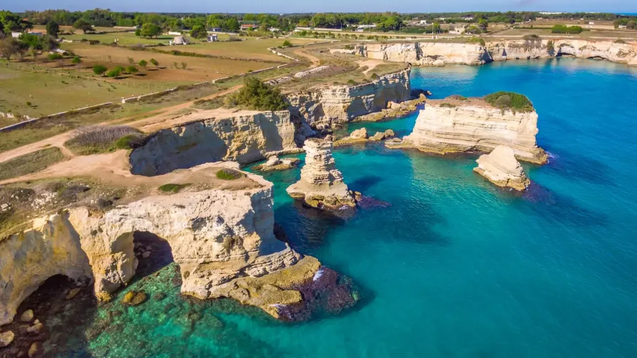 Scogliere bianche e mare turchese in una splendida **Puglia estate**. Faraglioni emergono dall'acqua cristallina, un vero paradiso.