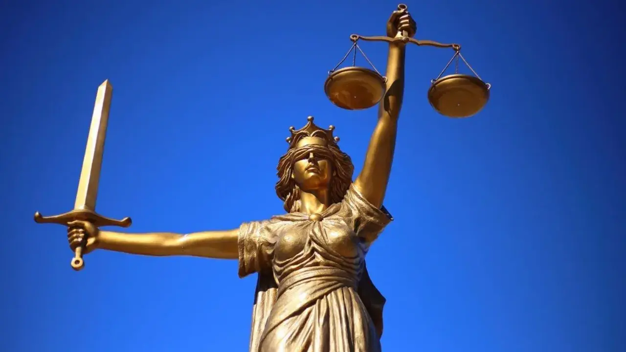Statua dorata della Giustizia con spada e bilancia, simbolo dei giudici ordinari, contro un cielo blu intenso.