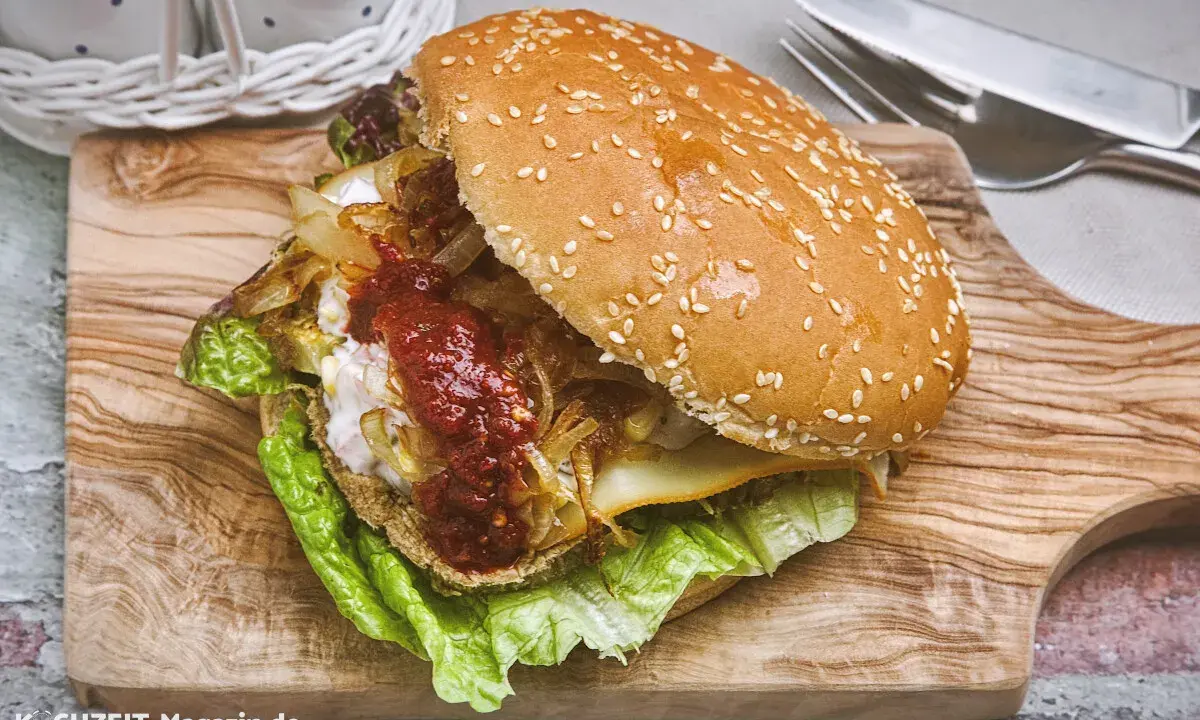 Ein saftiger vegetarischer Burger mit Salat, karamellisierten Zwiebeln und scharfer Sauce auf einem Holzbrett.