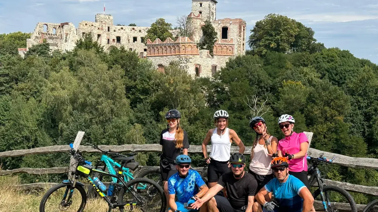Grupa rowerzystów na tle ruin zamku. Planują noclegi na Szlaku Orlich Gniazd rowerem.