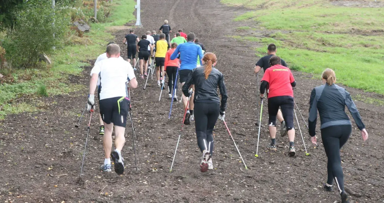 Grupp som går uppför en lerig backe med stavar, en aktivitet som liknar nordic walking.