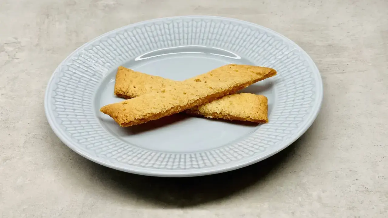 Två gyllene kolasnittar ligger korslagda på en ljusblå tallrik. Perfekt för ett enkelt kolasnittar recept.