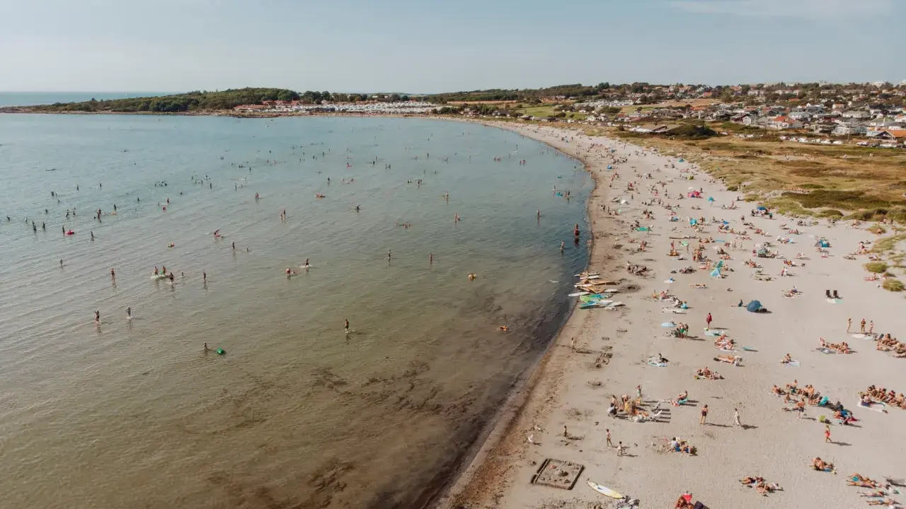 En livlig strand i Halland med många badande och solande människor. Vattnet är klart och inbjuder till lek.