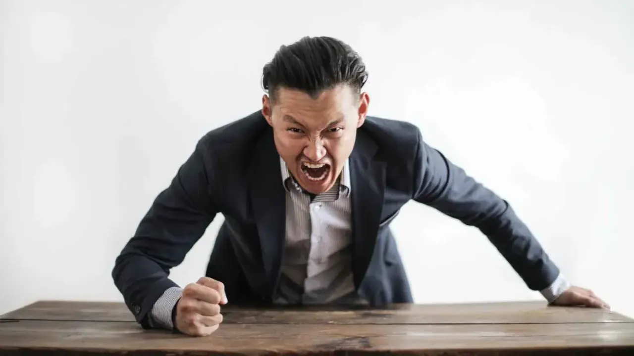 Wütender Mann im Anzug schreit über einen Tisch. Darf ein Lehrer Schüler anschreien?