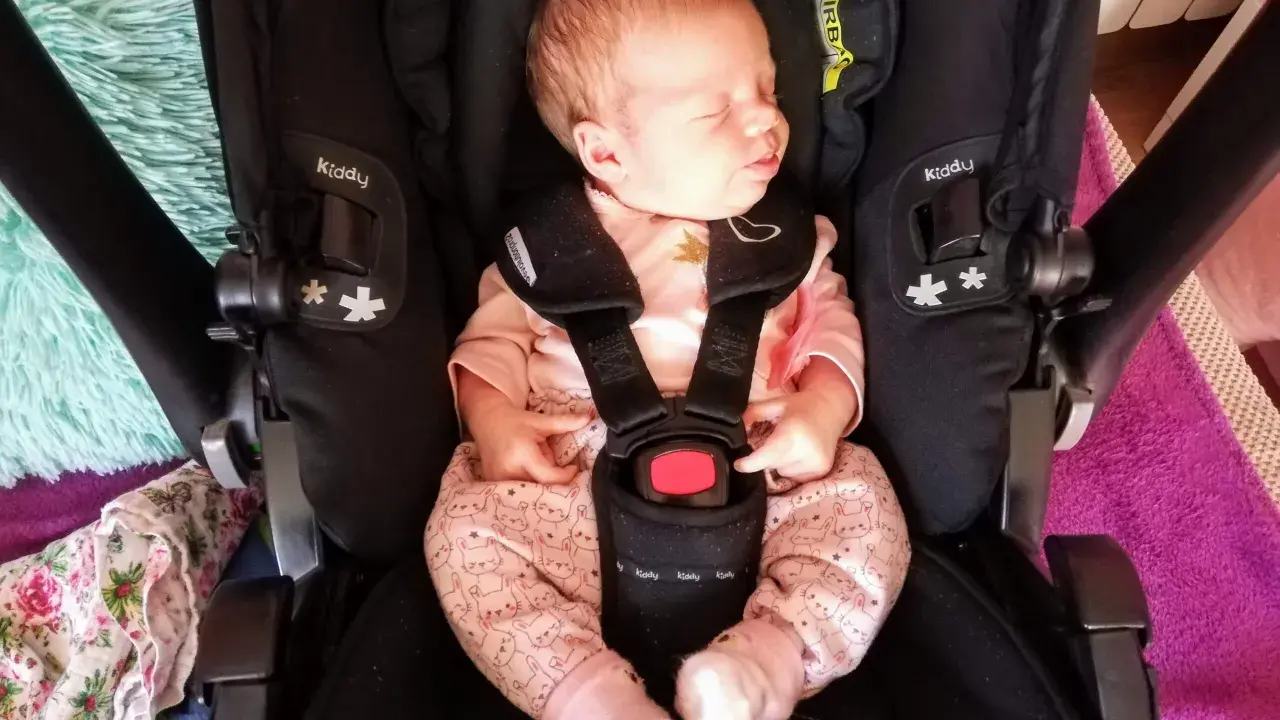Śpiący noworodek w różowym pajacyku z króliczkami w foteliku Kiddy. Wkładka noworodkowa zapewnia komfort i bezpieczeństwo.