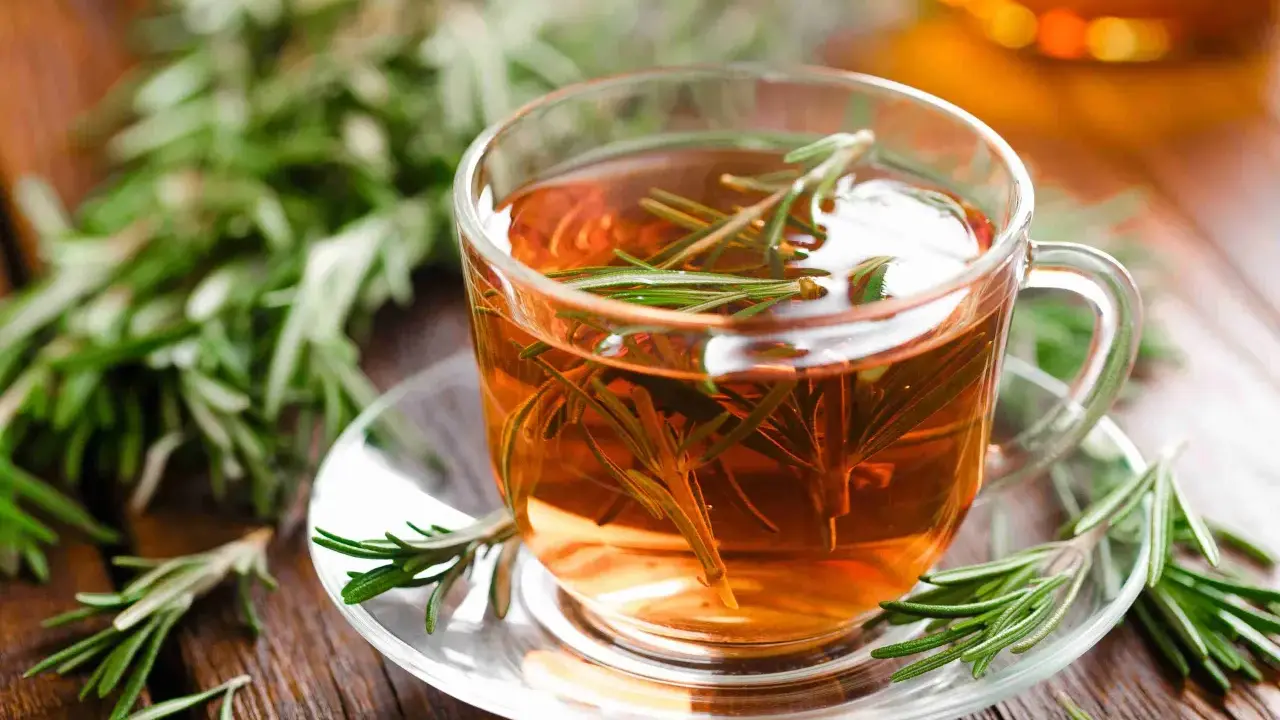 Une tasse de tisane romarin, avec des brins de romarin frais sur la soucoupe et en arrière-plan.