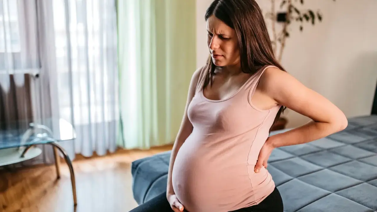 Schwangere Frau im 3. Trimester mit oberbauchschmerzen, hält sich den Rücken.