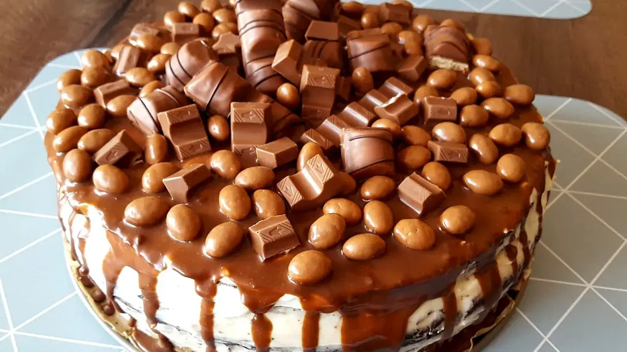 Pyszny tort kinder bueno, obficie udekorowany kawałkami batoników i czekoladowymi drażetkami, spływający karmelem.