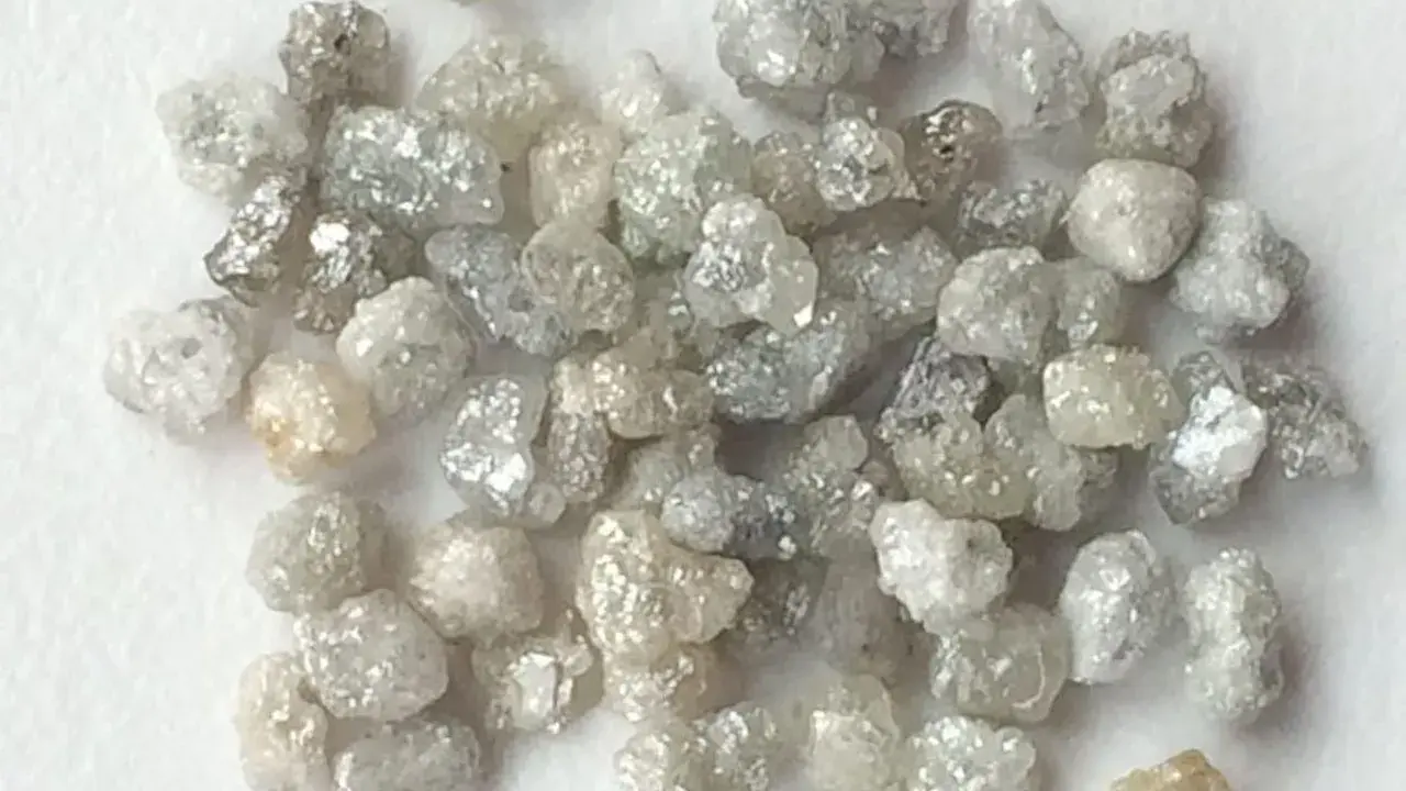 Un mucchio di grezzi diamanti non lavorati, con sfumature che vanno dal bianco al grigio e un leggero tocco dorato, pronti per essere trasformati.