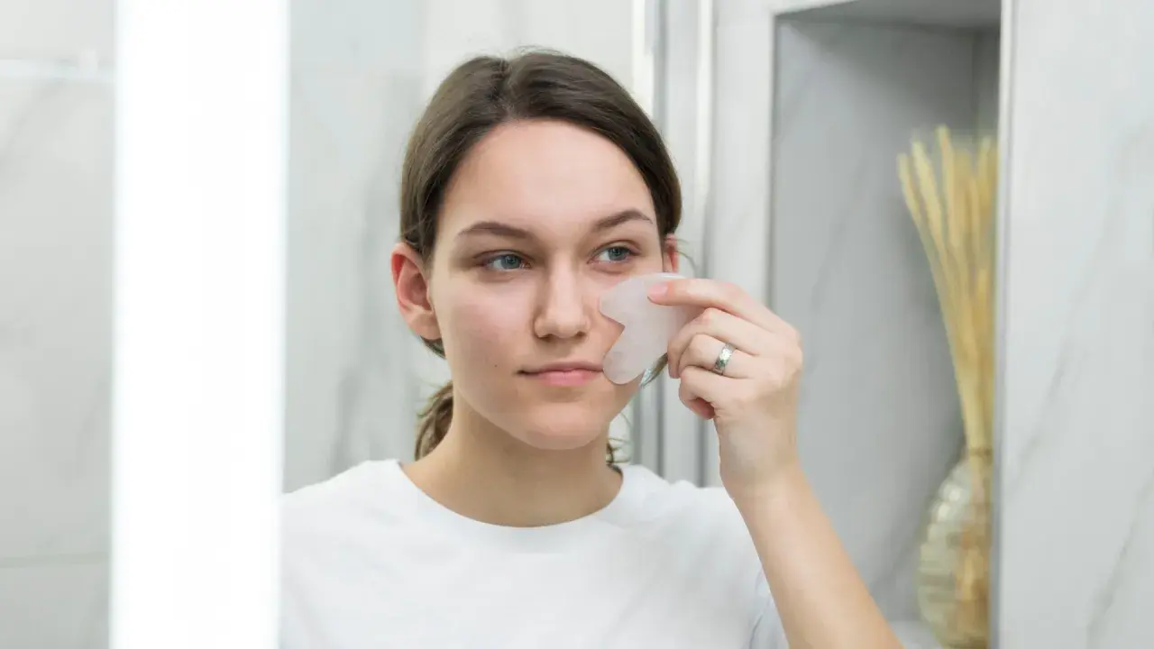 Une jeune femme utilise un gua sha pour un massage facial, un remède de grand-mère pour un visage gonflé.