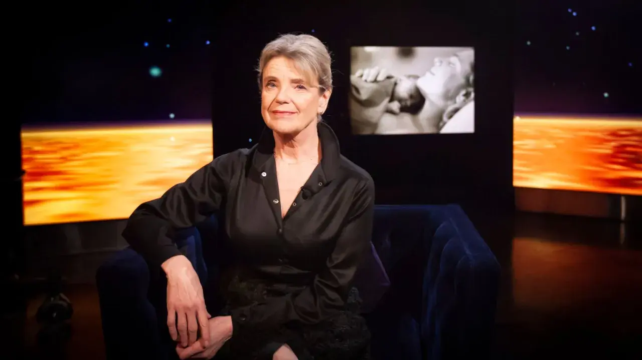 Stina Ekblad sitter i en mörkblå soffa, med en skärm bakom sig som visar klipp från filmer och tv-program med henne.