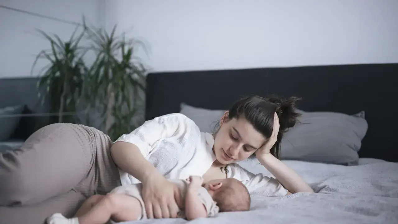 Mama karmi na leżąco swoje dziecko na łóżku. Czuły moment bliskości i spokoju.