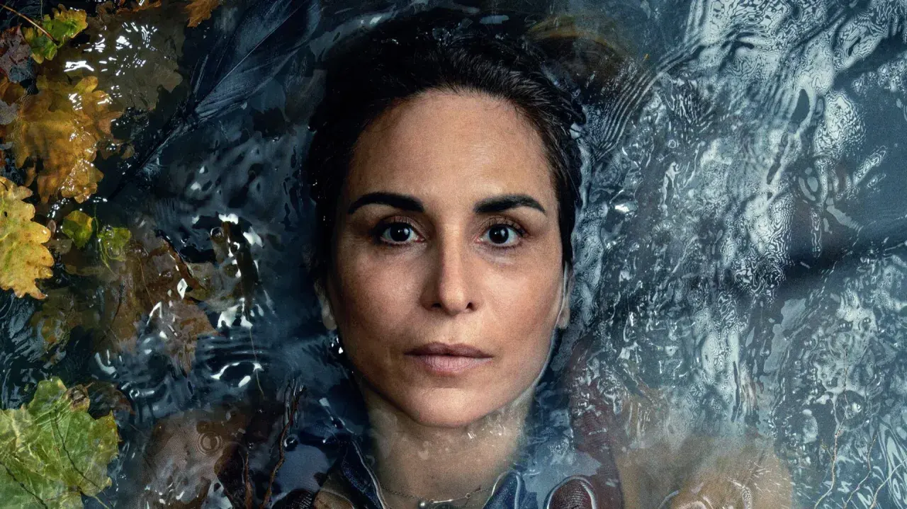 En kvinna med intensiv blick flyter i mörkt vatten, omgiven av höstlöv. En scen från veronica serie.