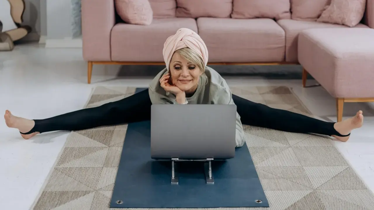 Kvinna i spagat framför laptop, med en rosa soffa i bakgrunden. Hon verkar lära sig om fosfor i kroppen.