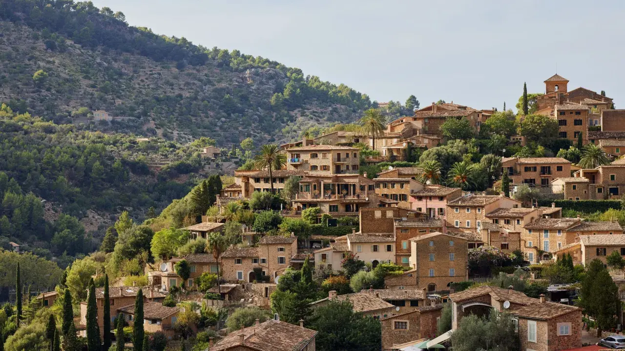 Mallorquinisches Dorf mit Steinhäusern und Terrassen an einem bewaldeten Hang.