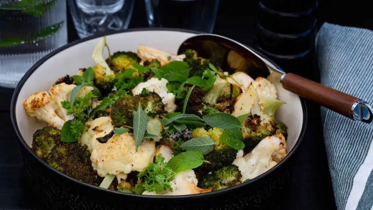En skål med ugnsrostad blomkål och broccoli, toppad med färska örter. Perfekt som tillbehör till middagen.
