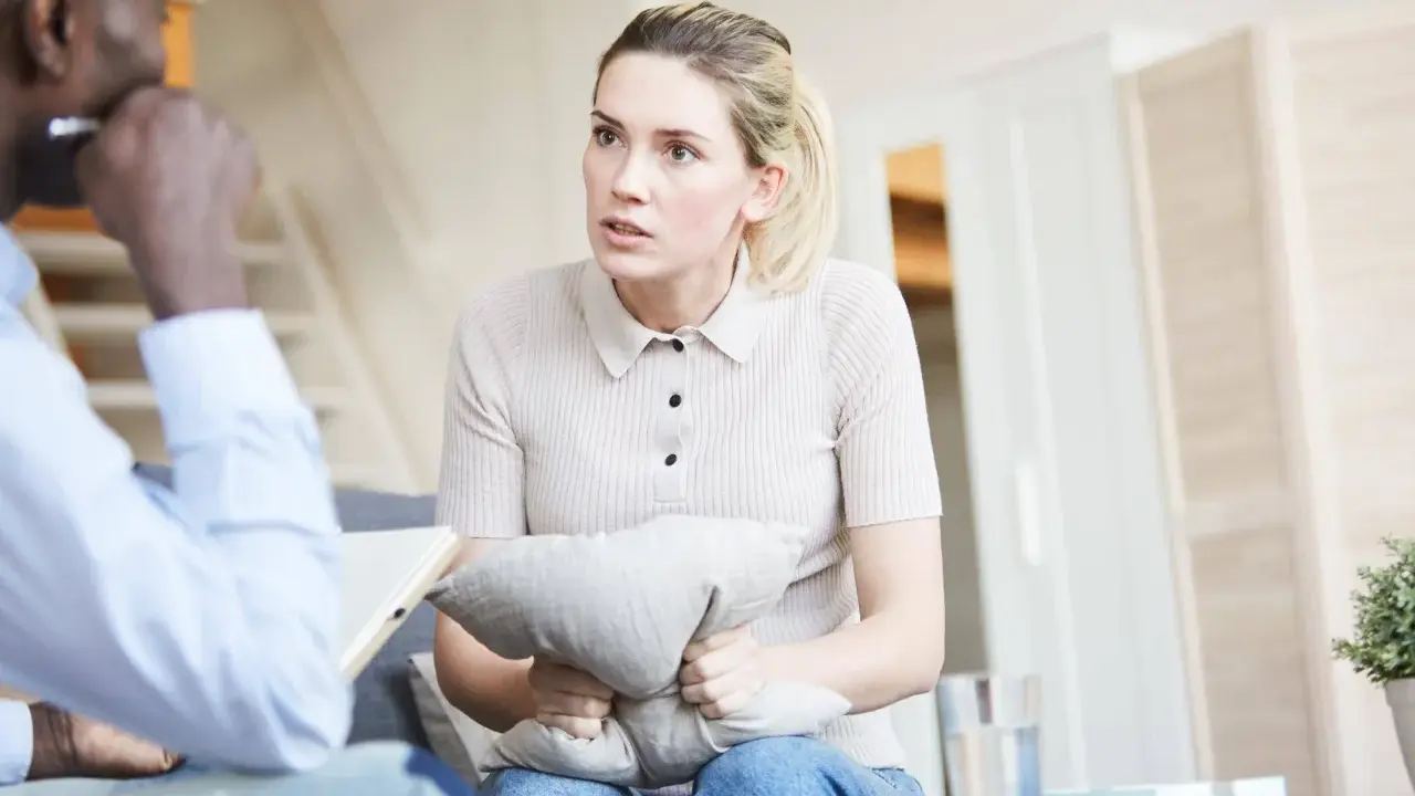 Kobieta trzyma poduszkę, rozmawiając z terapeutą. Czeka na zwolnienie od psychiatry, by móc wrócić do normalnego życia.