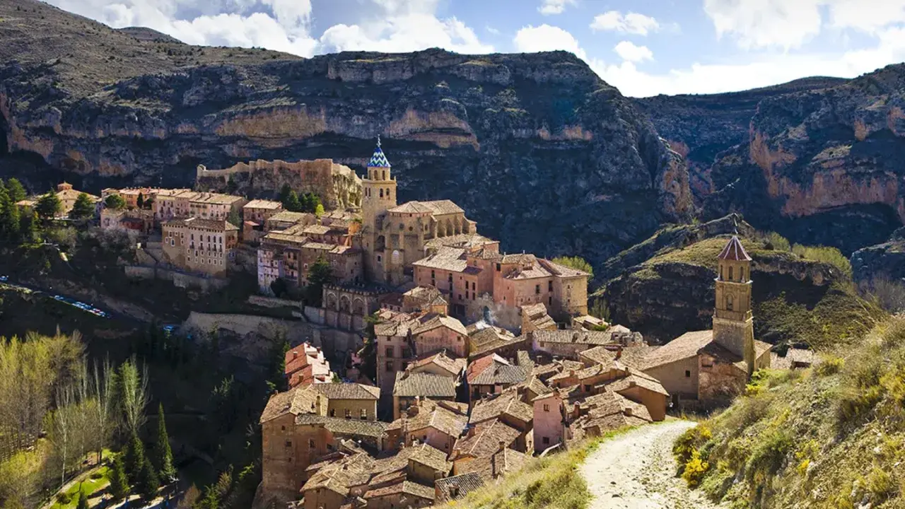 Malerisches Dorf Albarracín, Spanien, schmiegt sich an steile Felsen. Ein Weg führt durch grüne Hügel zum historischen Ortskern.