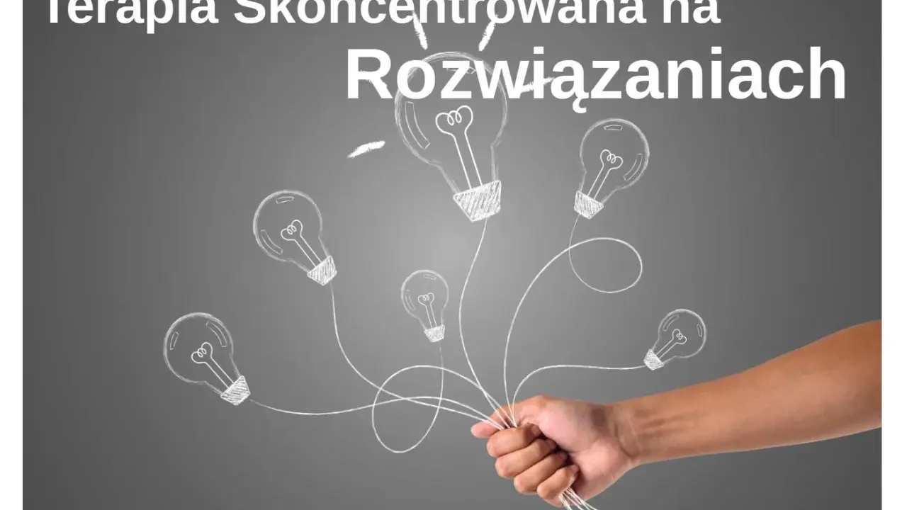 Dłoń trzymająca pęk żarówek narysowanych kredą na szarym tle.