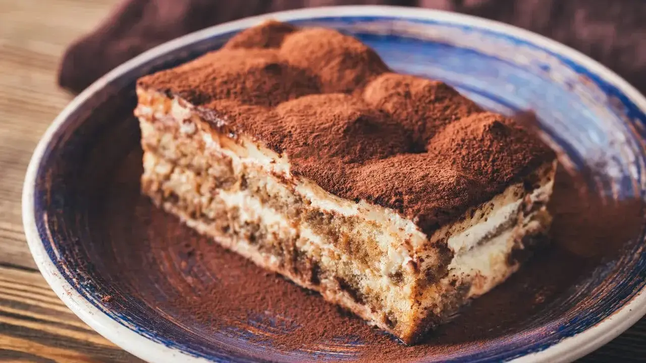Pyszny kawałek tiramisu z mascarpone, posypany kakao, na talerzu. Idealny sprawdzony przepis na deser.