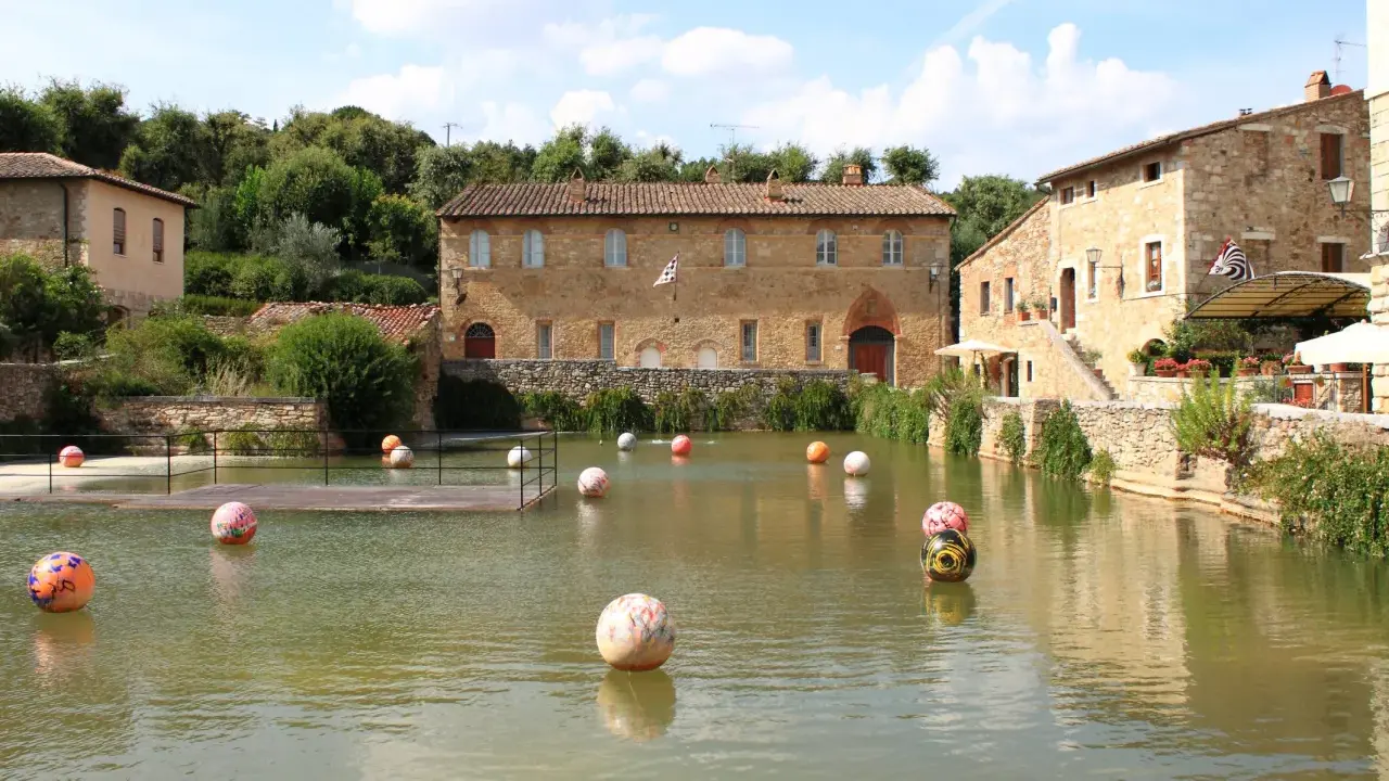 Paesini puglia con un laghetto pieno di sfere colorate, circondato da antichi edifici in pietra e vegetazione rigogliosa.