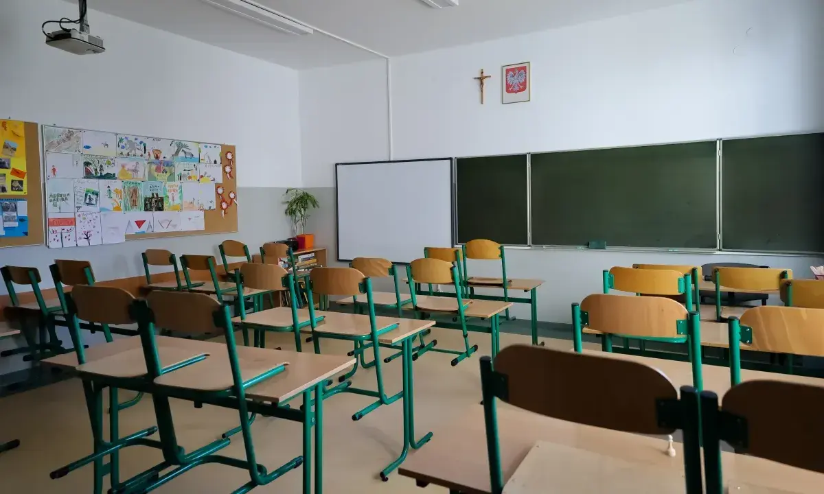 Pusta klasa szkolna z rzędami ławek i krzeseł. Na ścianie tablica, projektor i dziecięce rysunki. Wygląda na to, że **odwołane zajęcia w szkołach** sprawiły, że nikt dziś nie przyszedł.