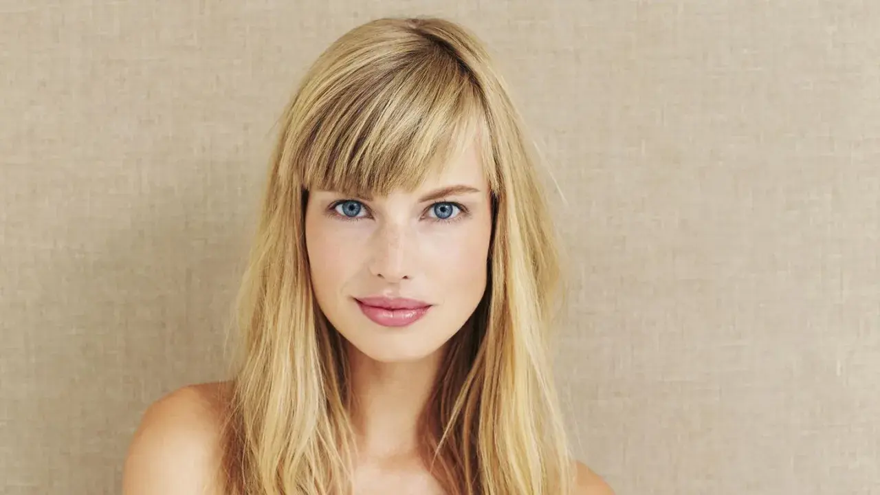 Blonde Frau mit blauen Augen und Pony. Eine Anleitung zum Pony schneiden könnte hier nützlich sein, um diesen Look zu erzielen.