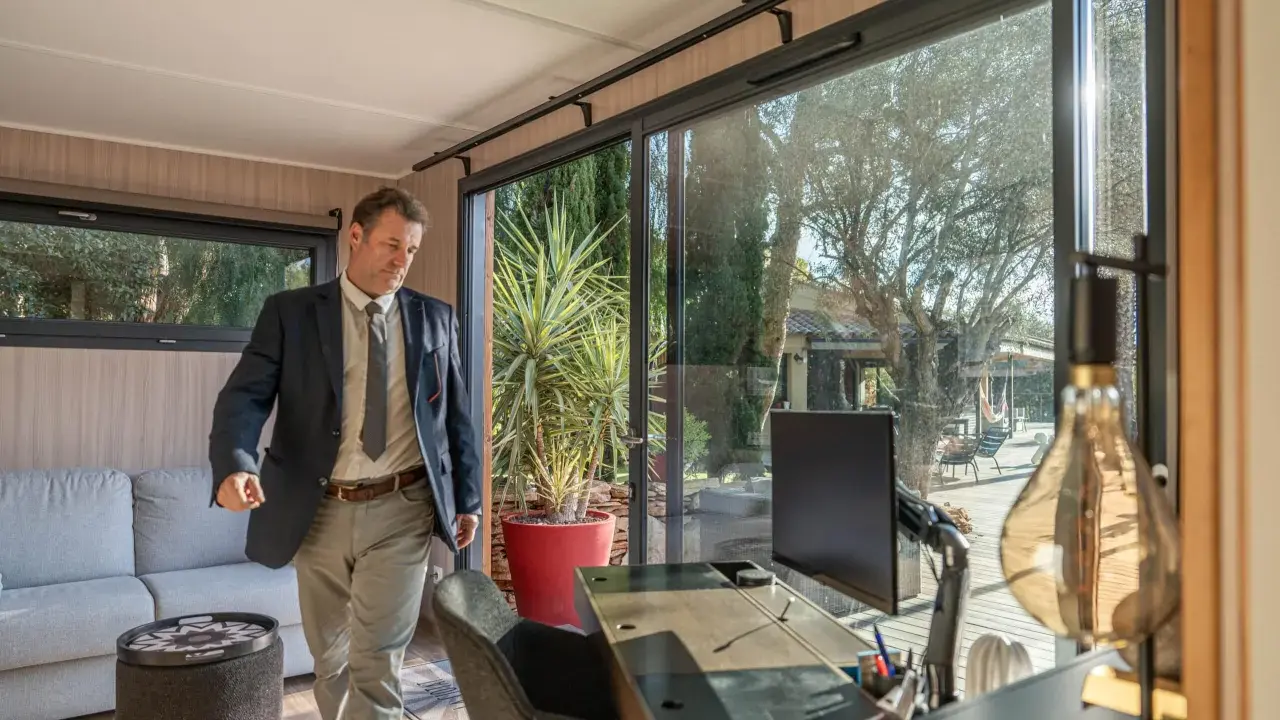 Un homme en costume entre dans un bureau lumineux avec vue sur un jardin. C'est la définition du home office : travailler depuis chez soi.