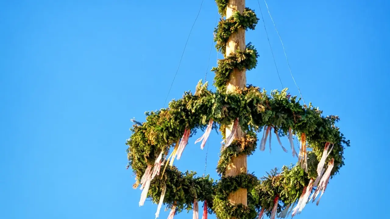 En midsommarstång, dekorerad med grönt och band, mot en klarblå himmel. Dess midsommarstång betydelse symboliserar sommarsolståndet och fruktbarhet.