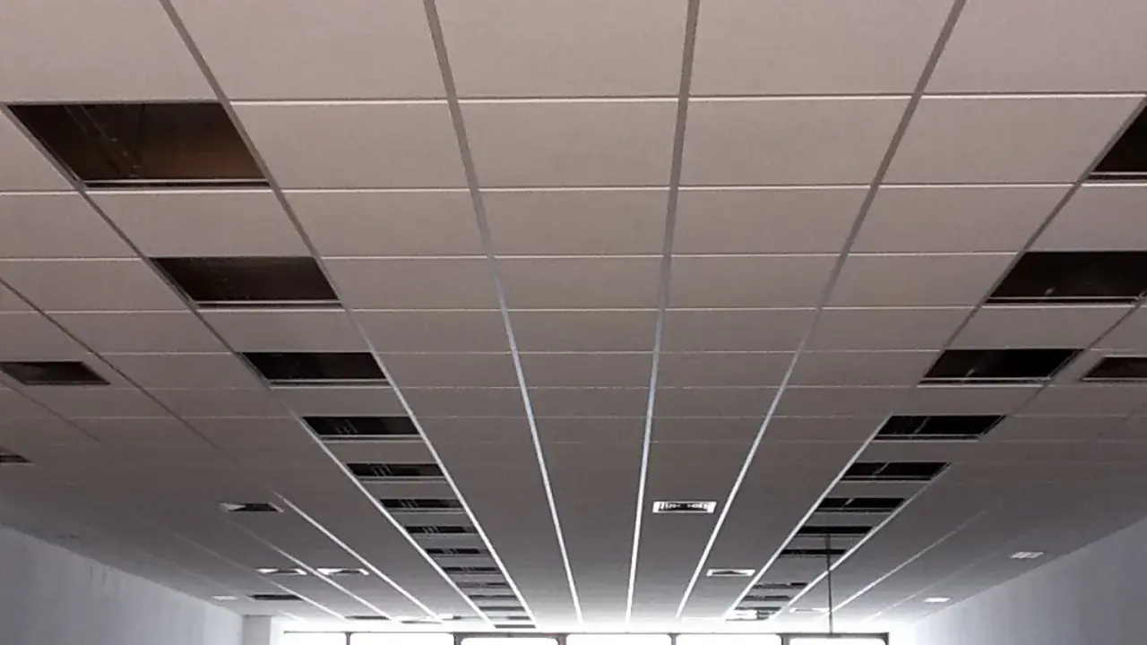 Instalación de un falso techo modular con paneles blancos y perfiles metálicos. Se aprecian huecos para iluminación o ventilación.