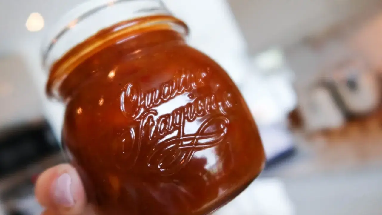 En hand håller ett glas med söt och syrlig rabarberchutney.