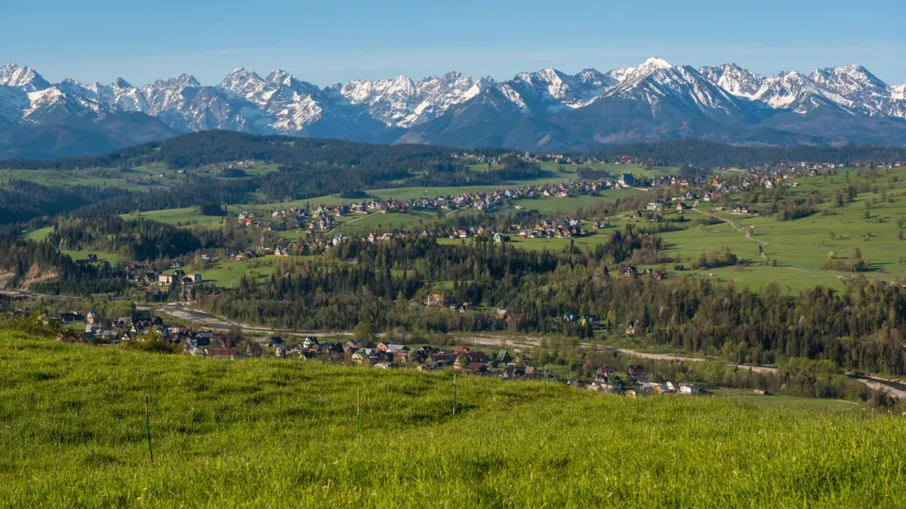 Widok na Tatry z zielonych wzgórz. W oddali widać zabudowania, które mogą być częścią trasy, ile km z Zakopanego do Bukowiny Tatrzańskiej.