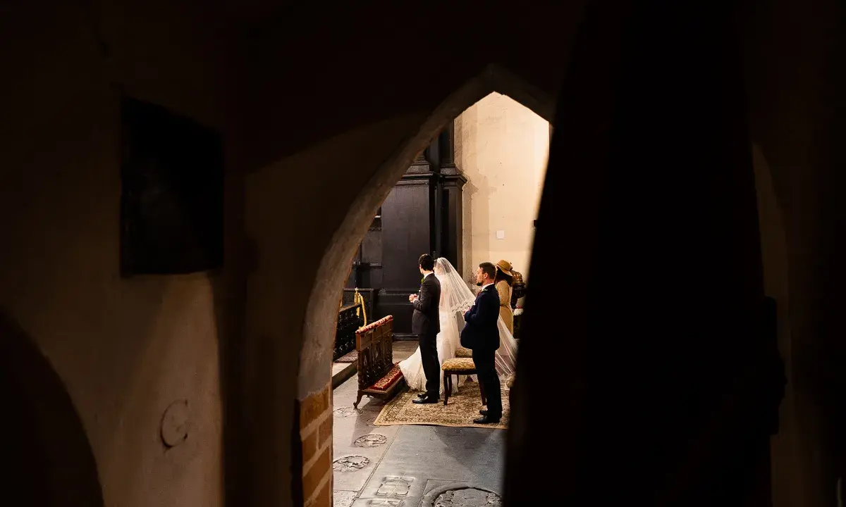 Ślub w kościele, para młoda i goście. Początkujący fotograf uchwycił ten magiczny moment zza ciemnego przejścia.
