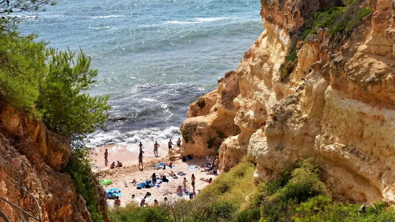 Sonnige Praia do Carvalho mit Felsen, grüner Vegetation und Badegästen am Meer.
