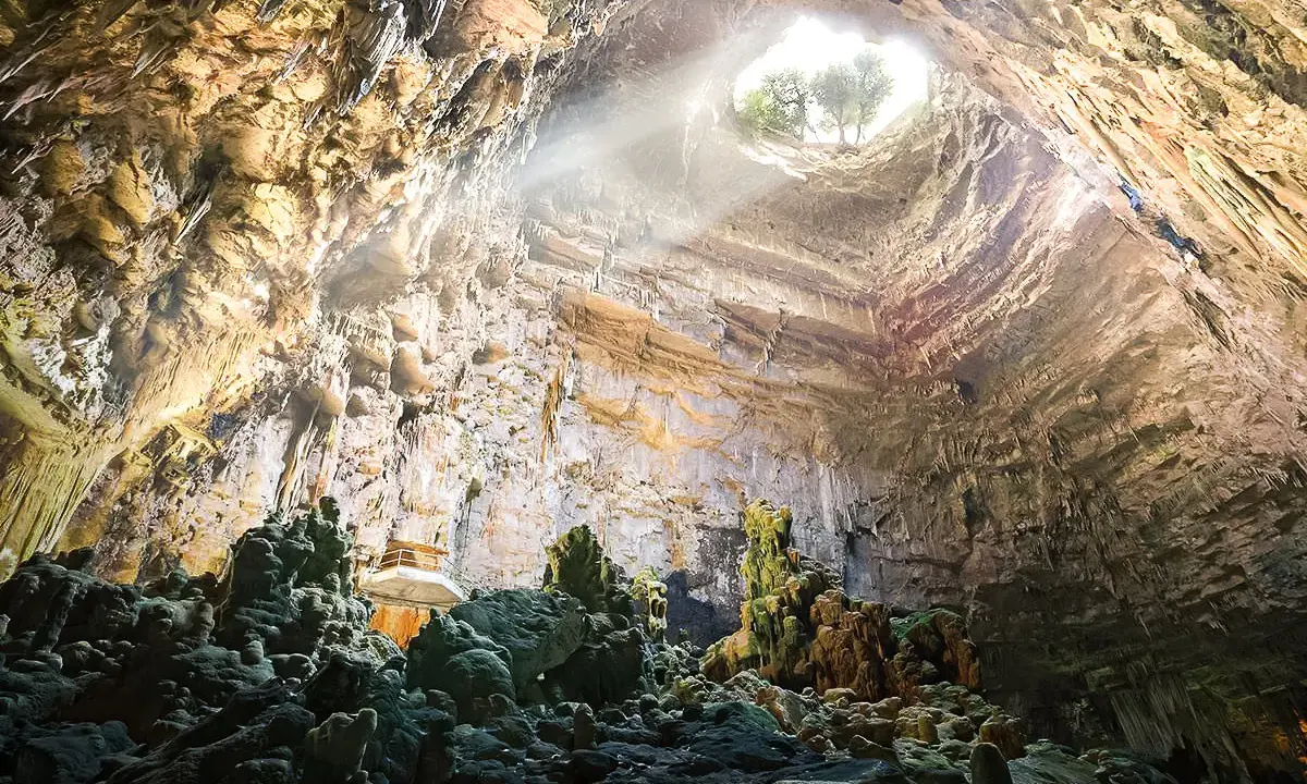 Grotta con stalattiti e stalagmiti illuminate da un raggio di sole. Un luogo magico da scoprire tra le cose da vedere vicino Alberobello.