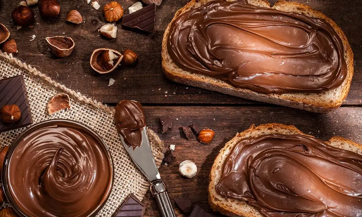 Selbstgemachte Haselnusscreme auf Brot, umgeben von Nüssen und Schokolade. Ein Genuss, der zum Nachmachen einlädt.