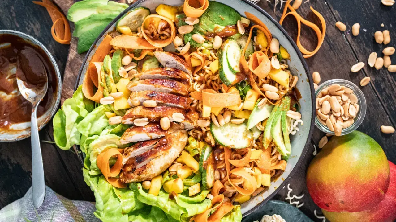 Ein bunter asiatischer Salat mit gegrilltem Hähnchen, Avocado, Mango, Karottenstreifen und Erdnüssen.
