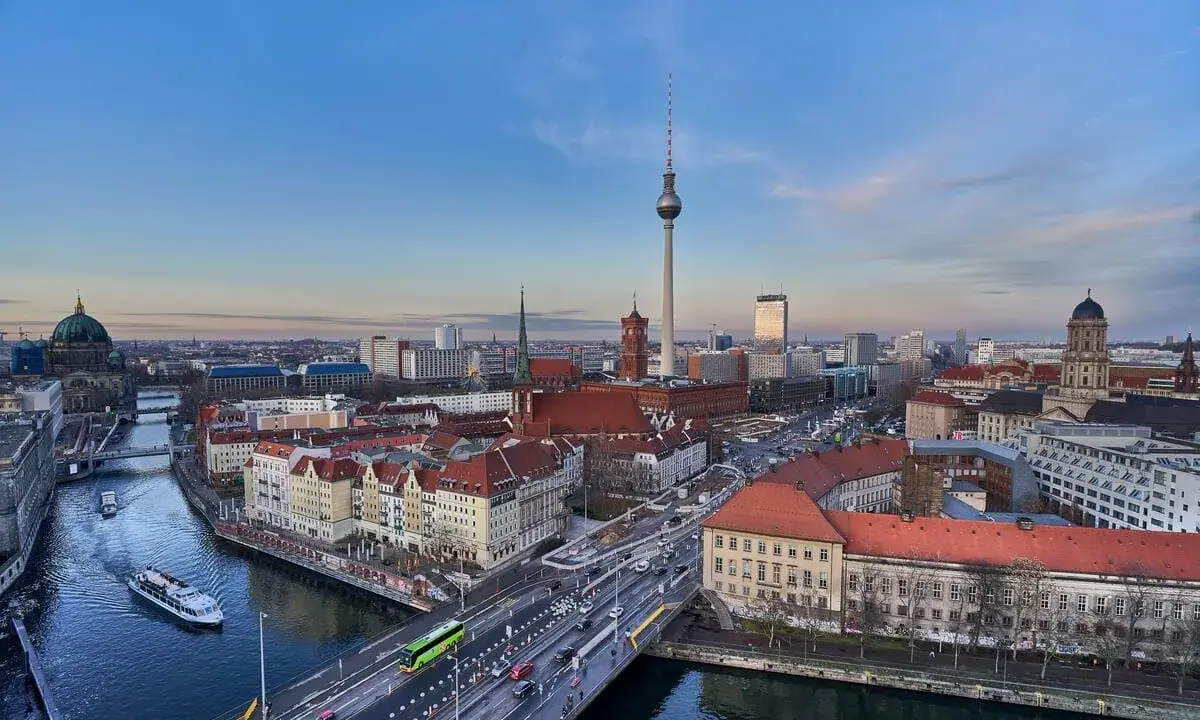 Ampio panorama berlino con la Torre della Televisione, il Duomo e il fiume Sprea. Traffico e barche animano la scena urbana.