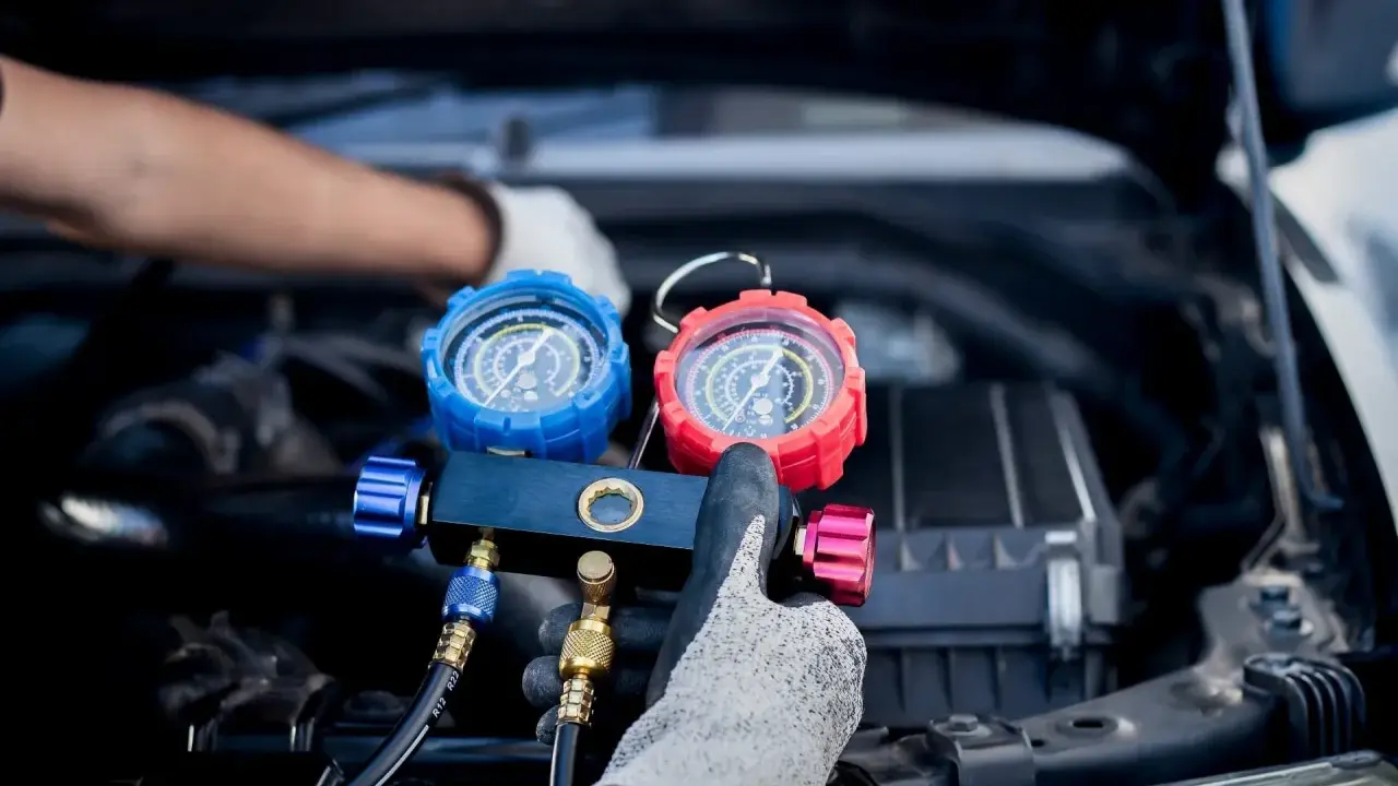Manos enguantadas ajustan manómetros para saber como cargar aire acondicionado coche.