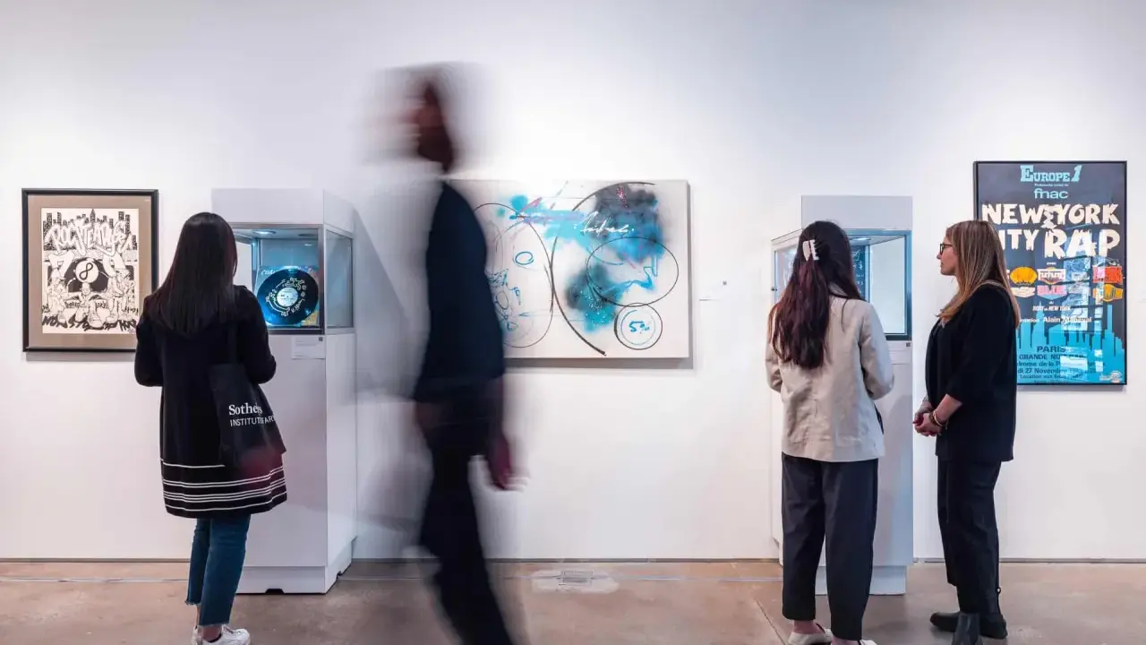 Visitors observe abstract art and a "New York City Rap" poster at a gallery exhibition.