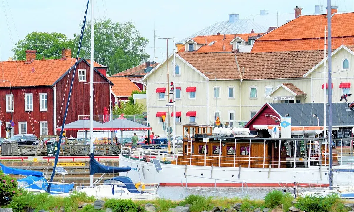 Båtar vid kajen framför hotell Vänerport i Mariestad. Röda och gula hus med tegeltak.