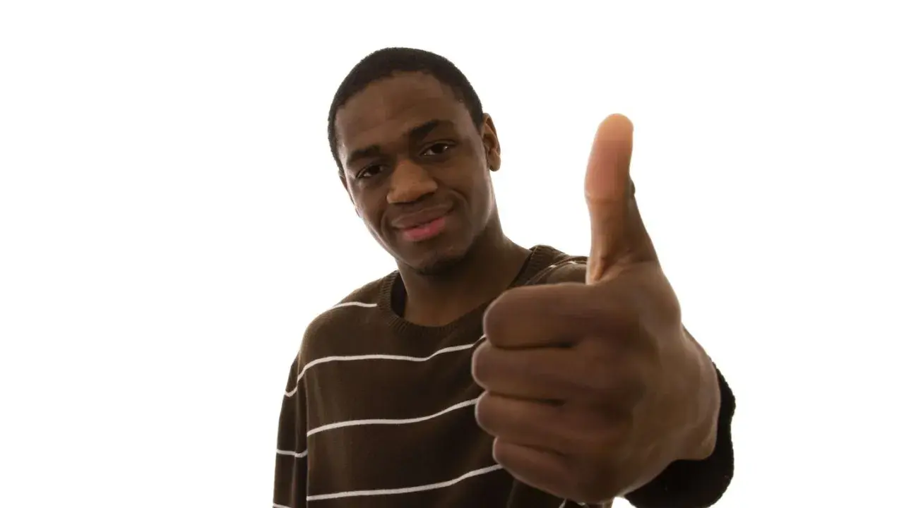 Un jeune homme souriant fait un pouce levé, un signe qui signifie "pas de soucis" ou "tout va bien".