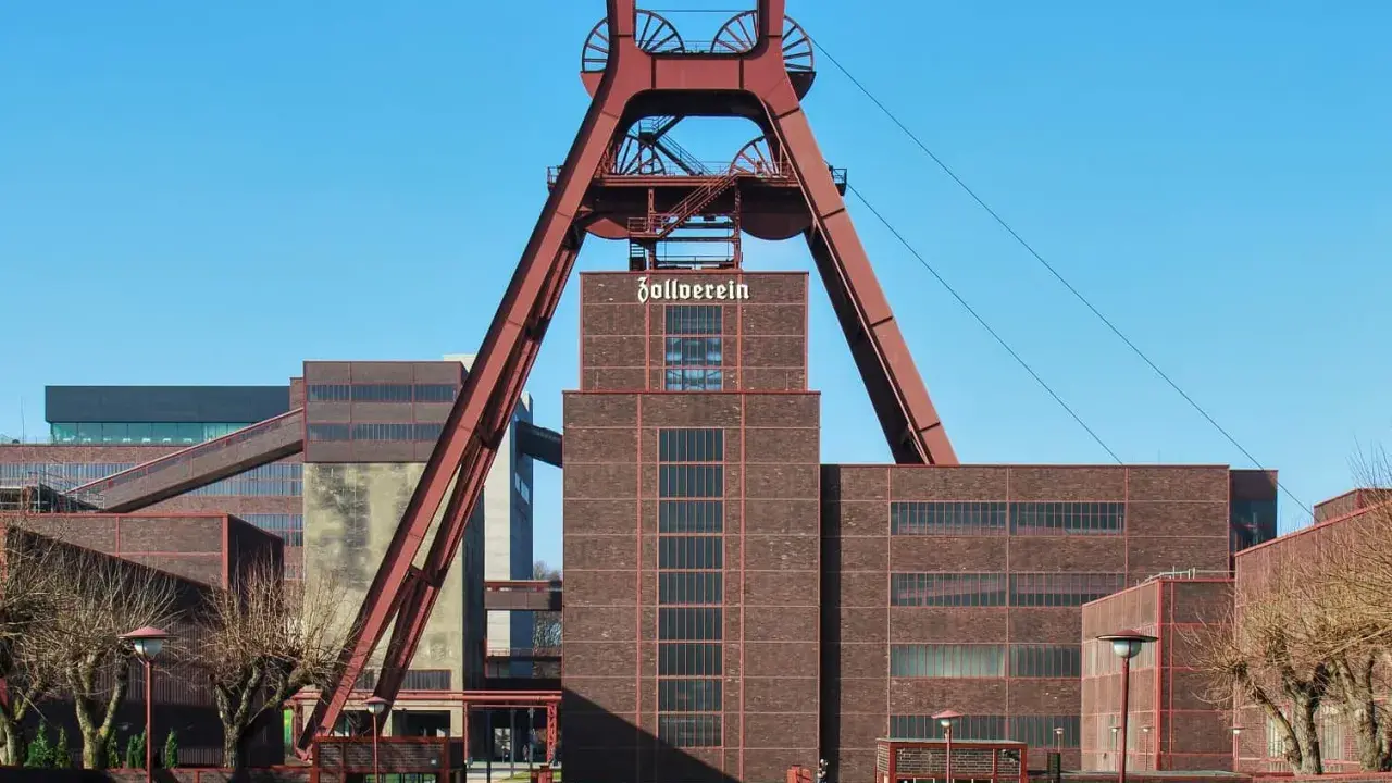 Industrielles Erbe mit rotem Förderturm und Backsteingebäuden. Die Zeche Zollverein strahlt eine starke, urbane Energie aus.