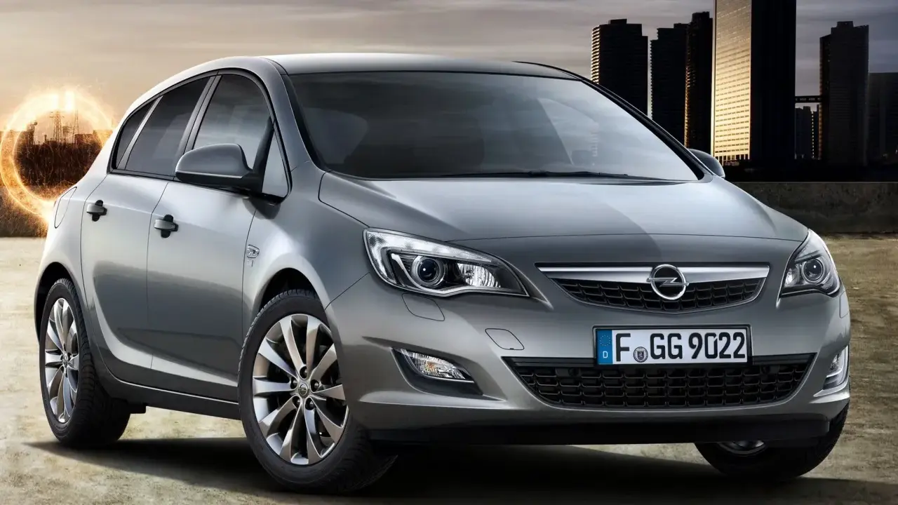 Szary Opel Astra 1.4 Turbo z nowoczesnymi światłami i felgami, na tle miejskiej panoramy i energetycznego kręgu.