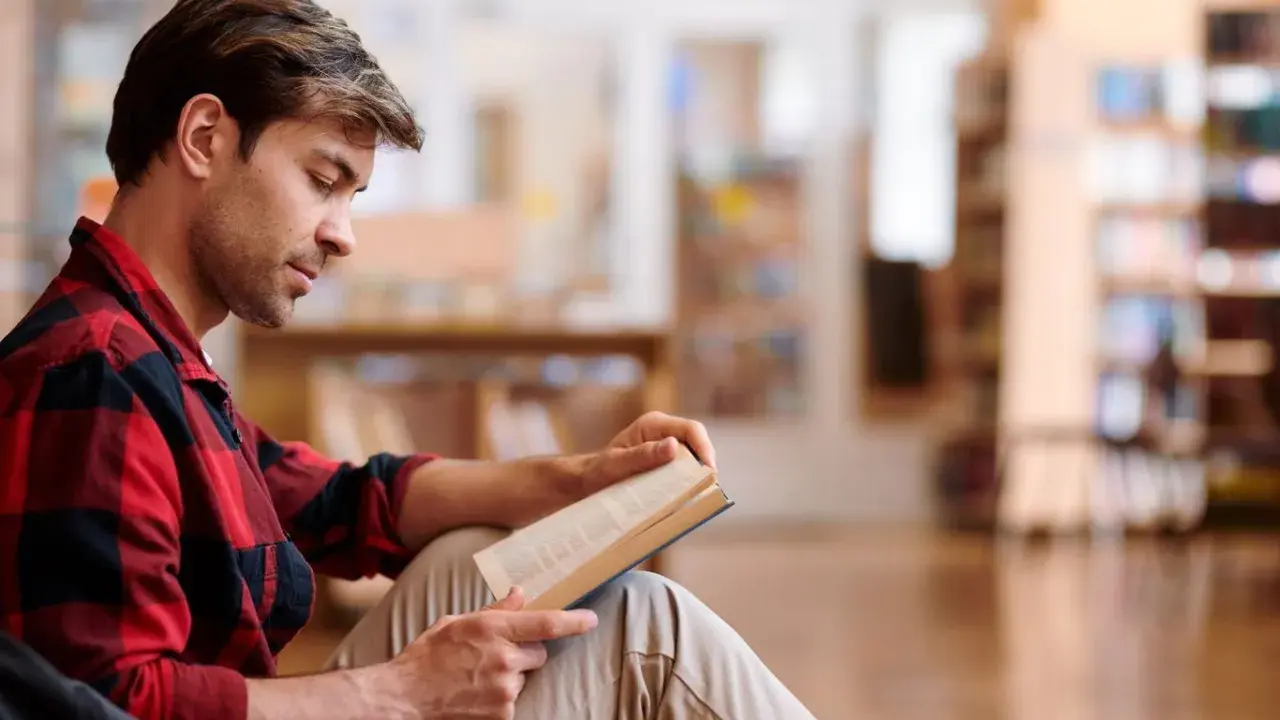 Mężczyzna w kratę czyta książkę w bibliotece.