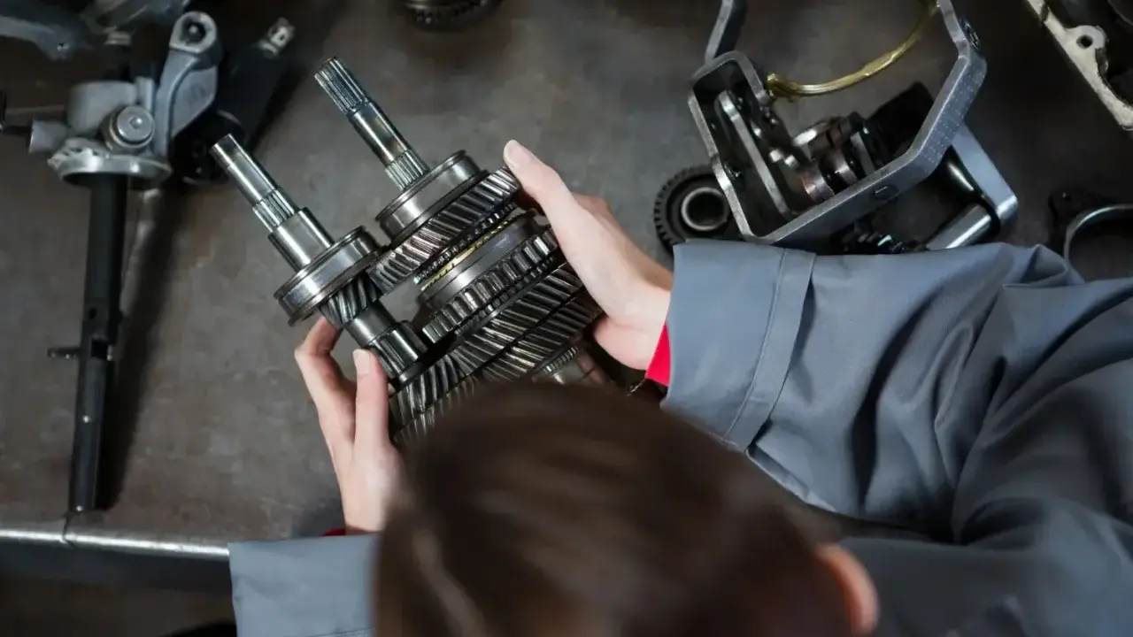 Mechanik trzyma wałki z zębatkami, przygotowując części samochodowe do wysyłki.